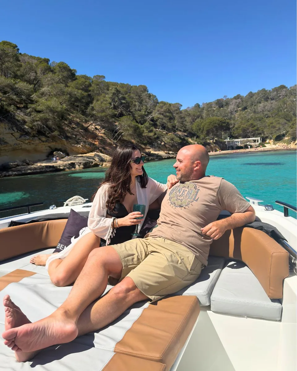 Pareja relajada en la proa de la barca fondeada en una cala turquesa